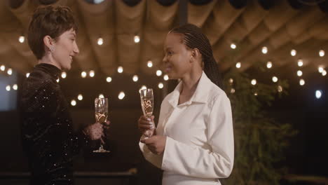 two elegant multiethnic women toasting and drinking champagne at new year's eve party 1