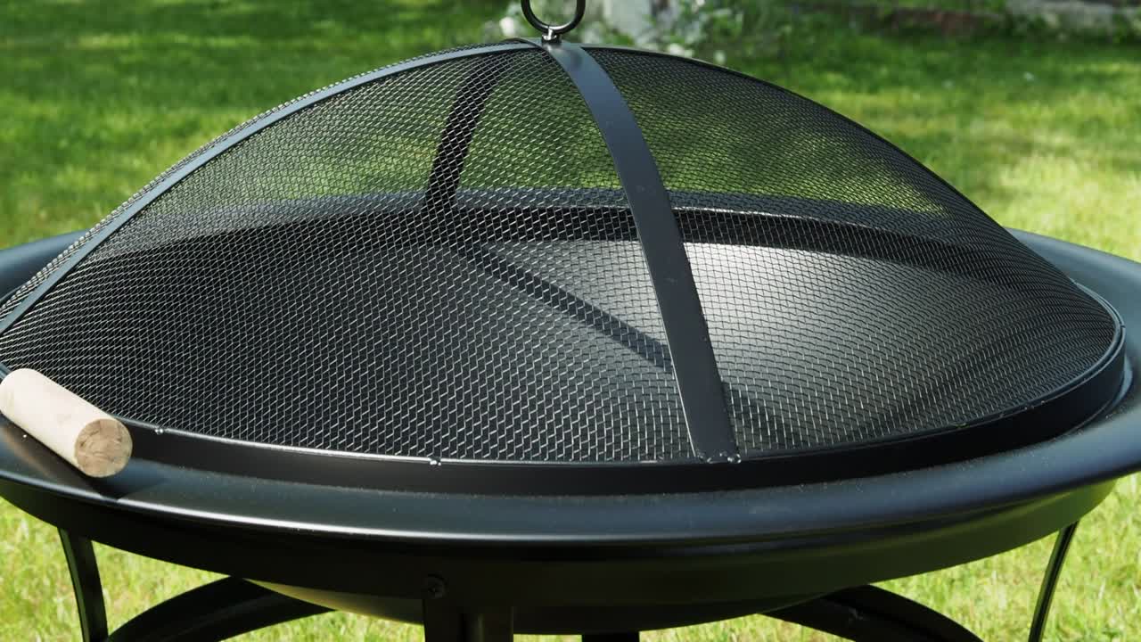 Metal bowl for fire on a background of green grass. Metal fire bowl with lid.