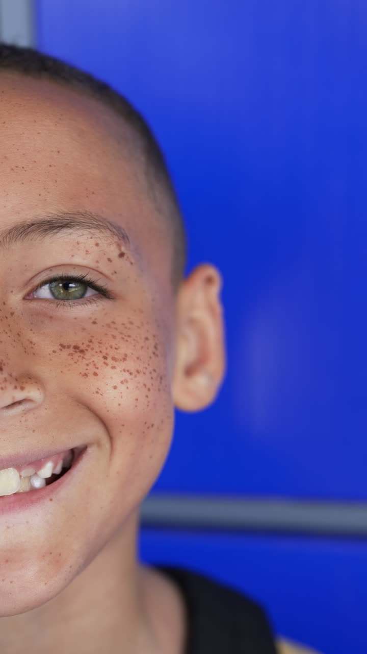 Vertical video: Smiling child with freckles in school, close-up of face with blue background