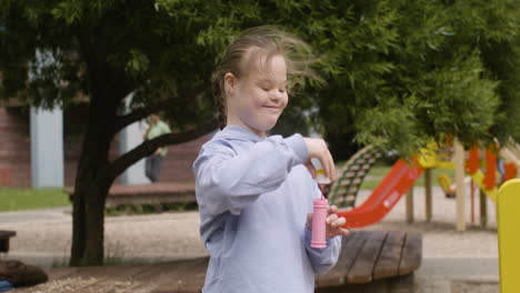 Kleines-Mädchen-Mit-Down-Syndrom,-Das-An-Einem-Windigen-Tag-Seifenblasen-Im-Park-Bläst