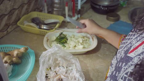 an asian lady pealing off garlic with the help of knife in the kitchen, close up view