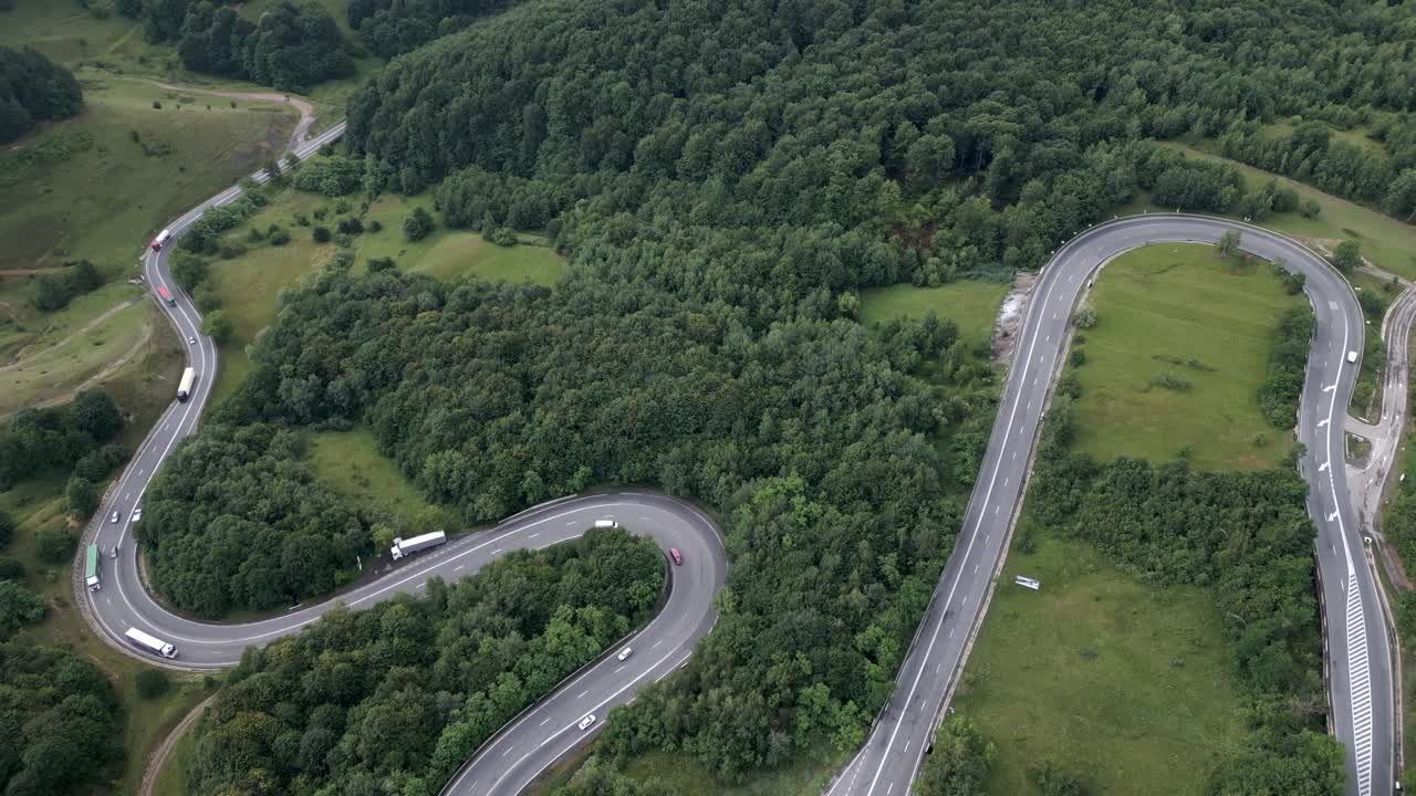 Tilt down aerial view of trucks on curved mountain road in lush Romanian forest
