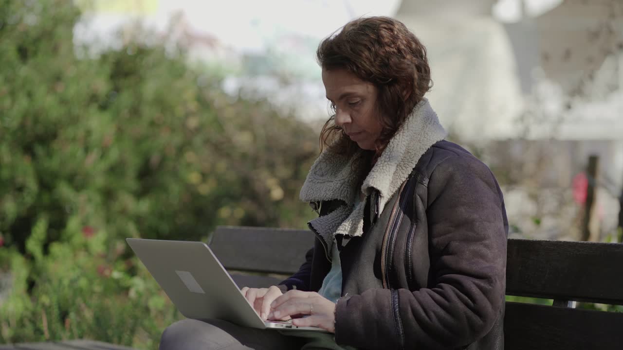 Focused curly female freelancer working with laptop outdoor