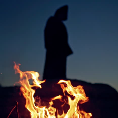 fire is burning on the dark background with black figure. scary atmosphere on halloween. ghost in black behind the vivid flame outdoors.