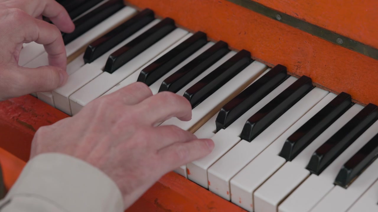 Close-up of hands playing worn orange piano keys with fingertips pressing and sliding across black and white key tops