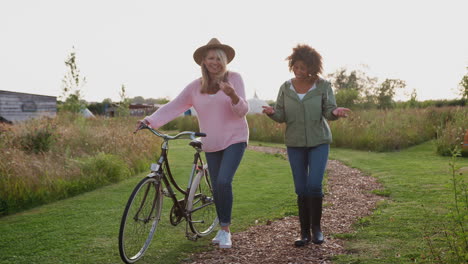 two mature female friends walking along path with bike through yurt campsite