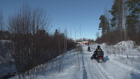 zwei schneemobile fahren auf einem weg mit bäumen auf beiden seiten, an einem kalten, sonnigen wintertag in schweden