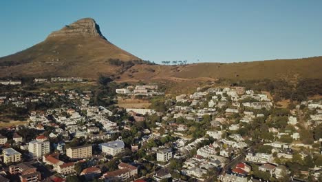 Drone-Volando-Sobre-Un-Barrio-Urbano-Con-La-Montaña-De-Cabeza-De-León-Al-Fondo-En-Ciudad-Del-Cabo,-Sudáfrica