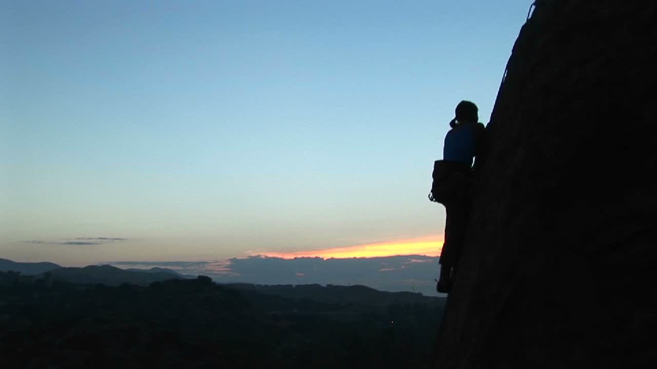 longshot de un escalador escalando un acantilado recortado contra un goldenhoursky