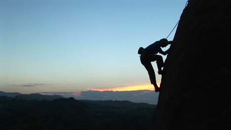 longshot of a rock climber scaling a cliff silhouetted against a goldenhoursky