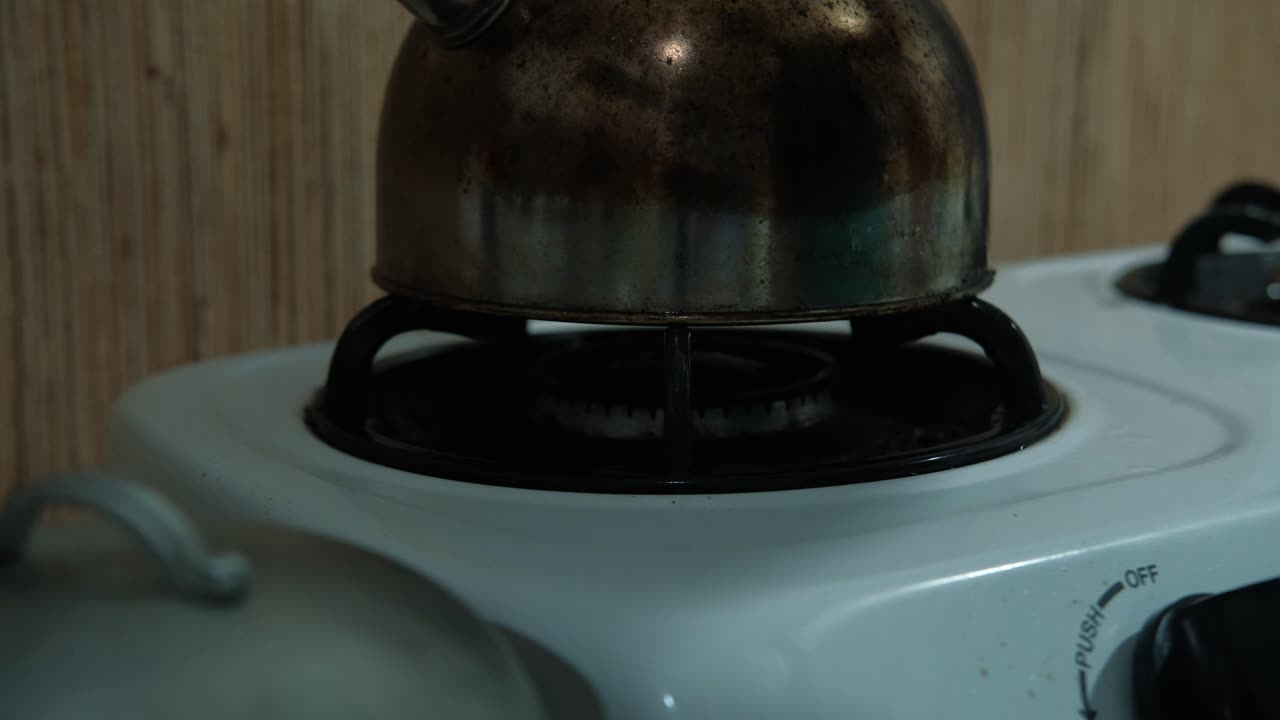 Stovetop burner igniting with water kettle above it. -Static closeup shot