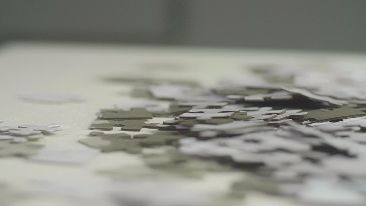 White and gray puzzle pieces laying randomly on a white surface. Smooth camera sliding movement.