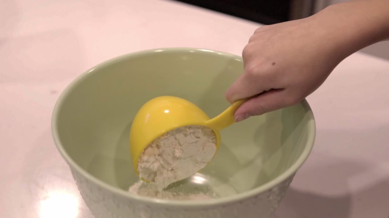Slow motion of flour pouring from a measuring cup into a large bowl
