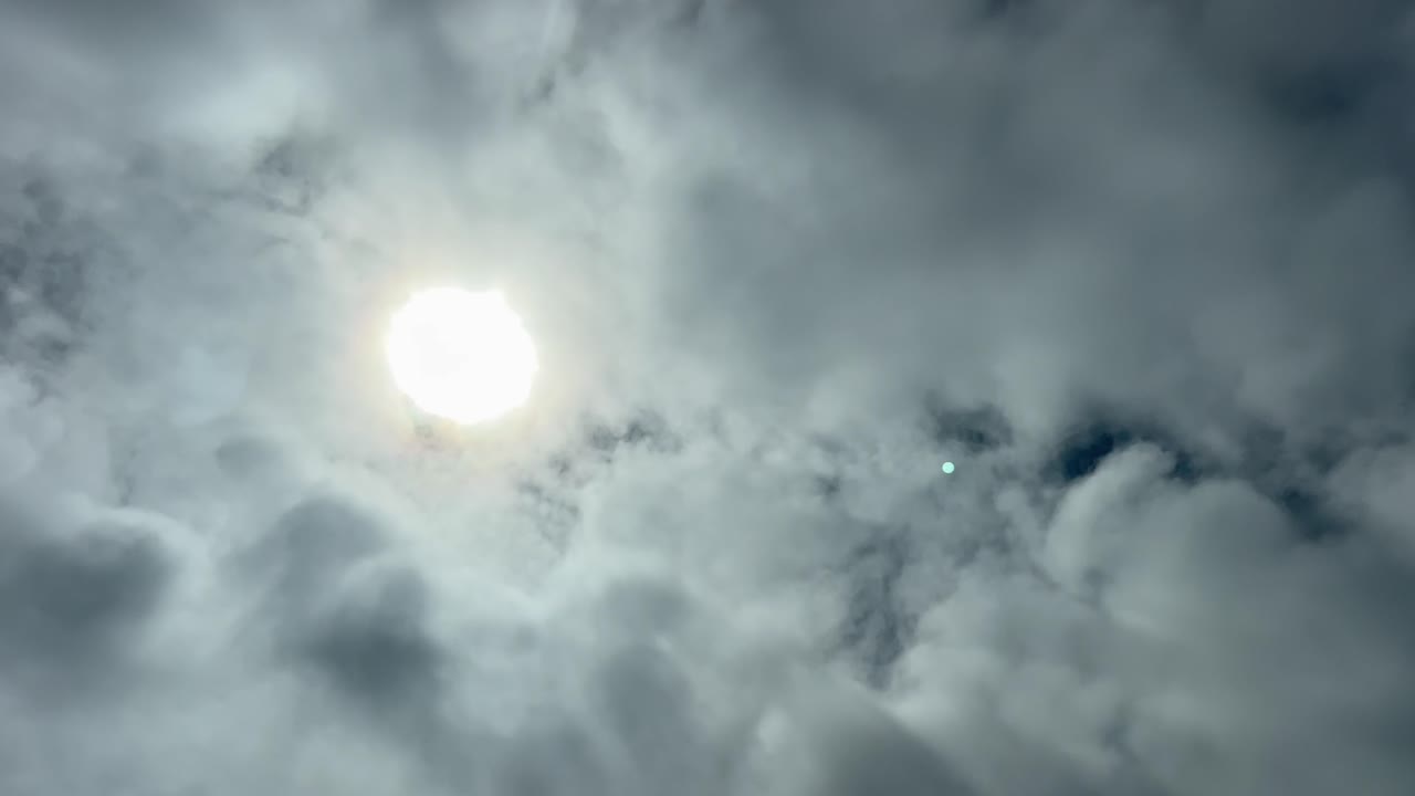 Pilot POV FPV of a veiled shining sun partially hidden by a thin layer of stratus clouds. Aerial footage taken from an airplane cockpit in a real time flight. 4K 60FPS