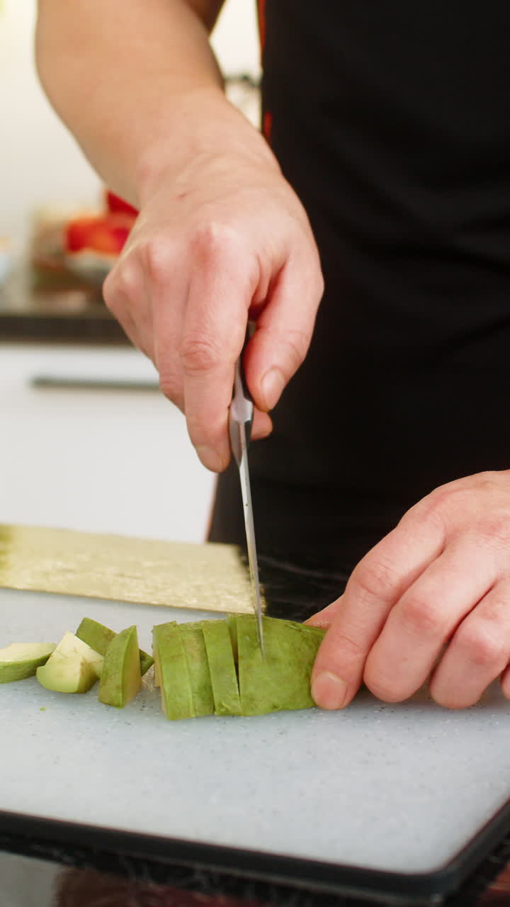 Man slicing avocado on cutting board in home kitchen preparing healthy balanced meal for clean diet