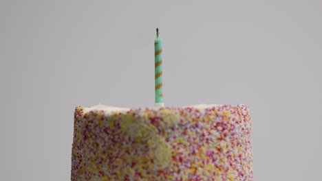 lit single candle on studio shot of revolving birthday cake covered with decorations being blown out 1