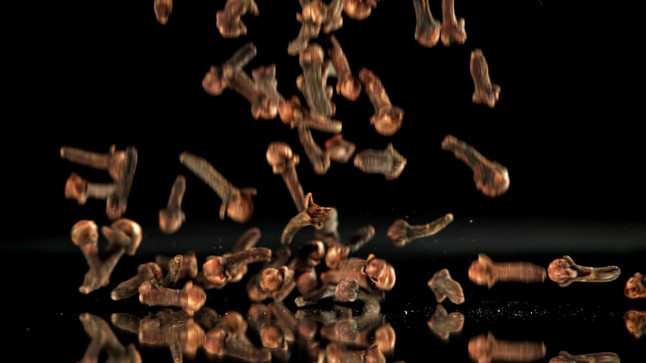Whole Dried Cloves Falling in Slow Motion on Black Background