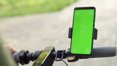 closeup of electric scooter hand tapping with his finger on chromakey screen of smartphone. tourist on electric scooter uses phone with green screen