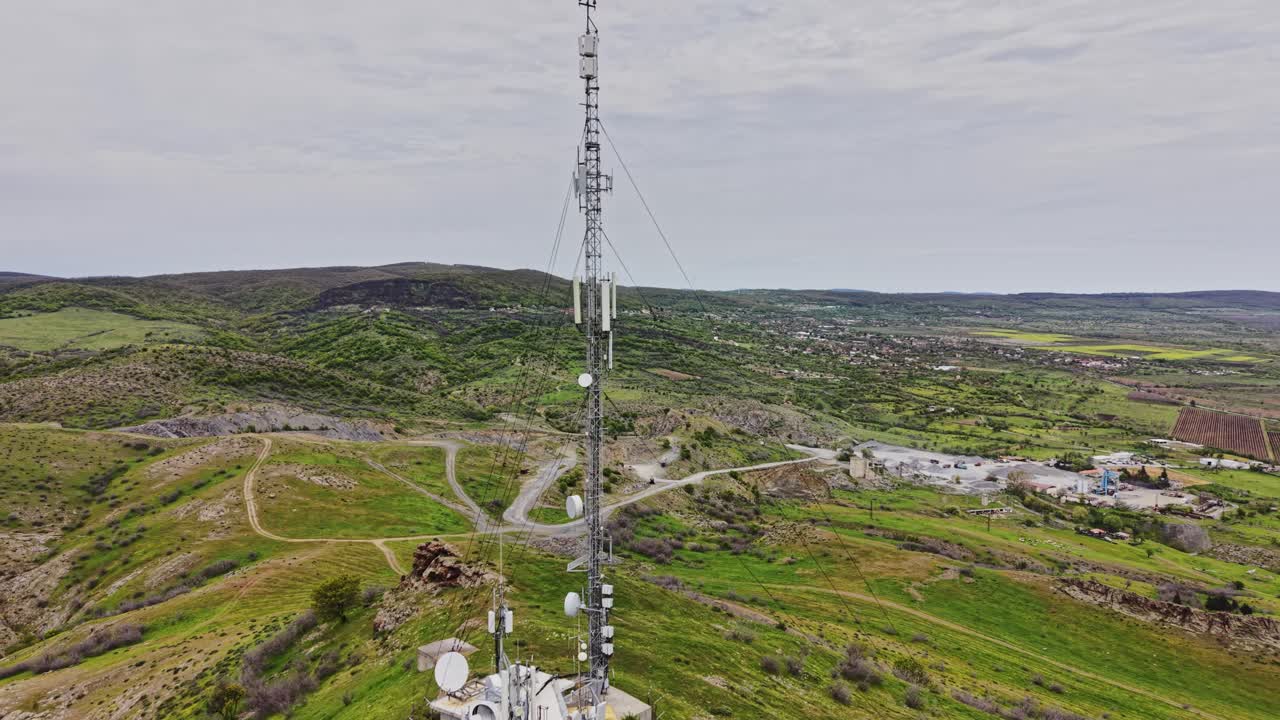 Una torre di comunicazione si erge su una collina che domina campi verdi in primavera.