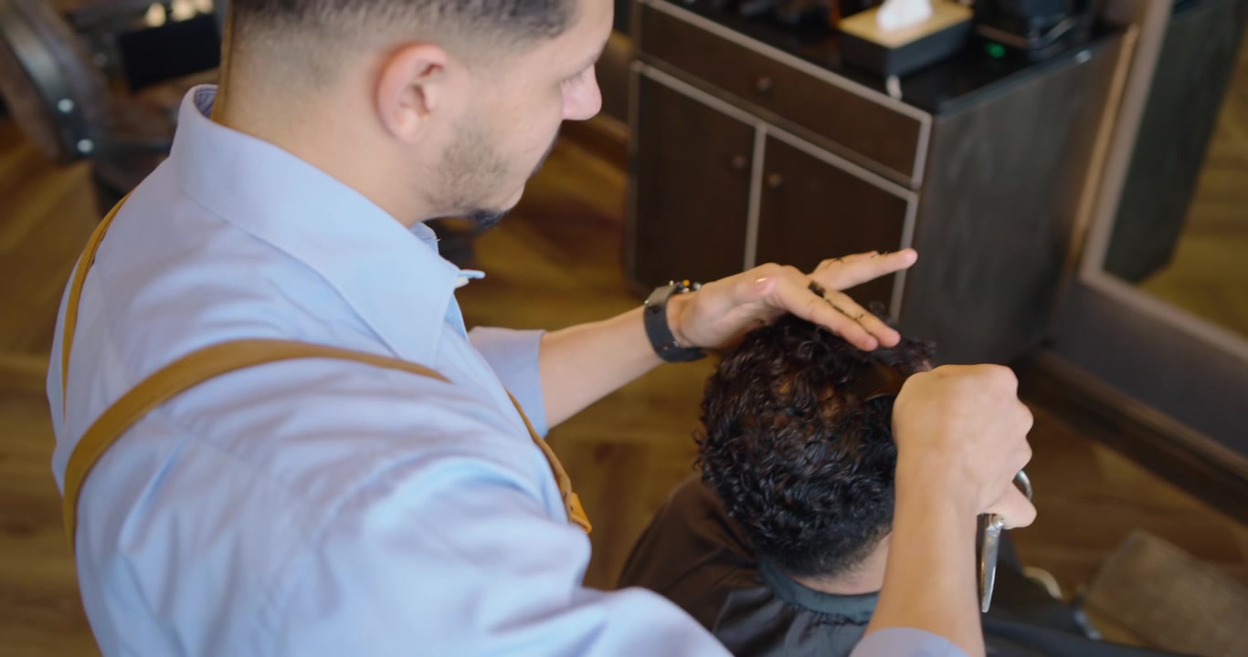 Afroamerikansk mandlig frisør reder hår og klipper med saks i salonen efter kundens ønske.