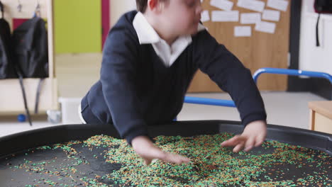 primary schoolboy with down syndrome stands using a sensory play tub in a classroom, close up