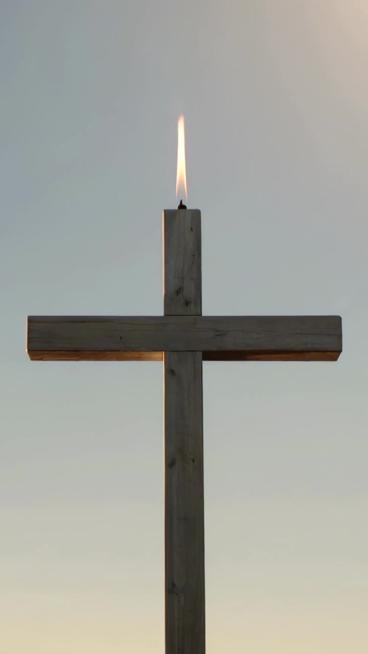 Vertical video: Recording wooden cross with wick, flame flickering and shifting outdoors at sunset