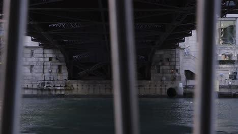 underside of a large bridge over water, viewed through vertical bars