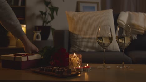 hombre planeando una velada romántica en casa en el salón con regalo de chocolates de vino y rosas 1