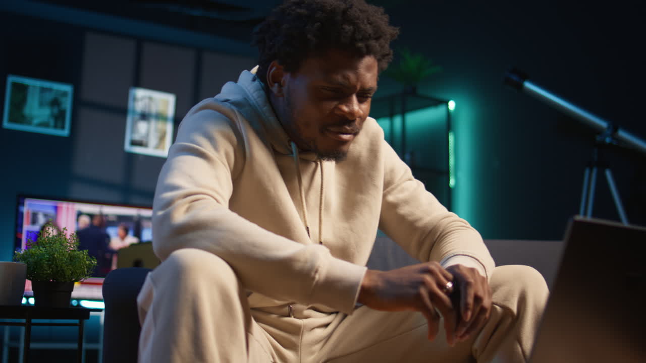 Independent black man using laptop for remote job tasks on a coffee table, surrounded by notes and enjoying the benefits of schedule flexibility. Embracing the modern freelance work. Camera B.