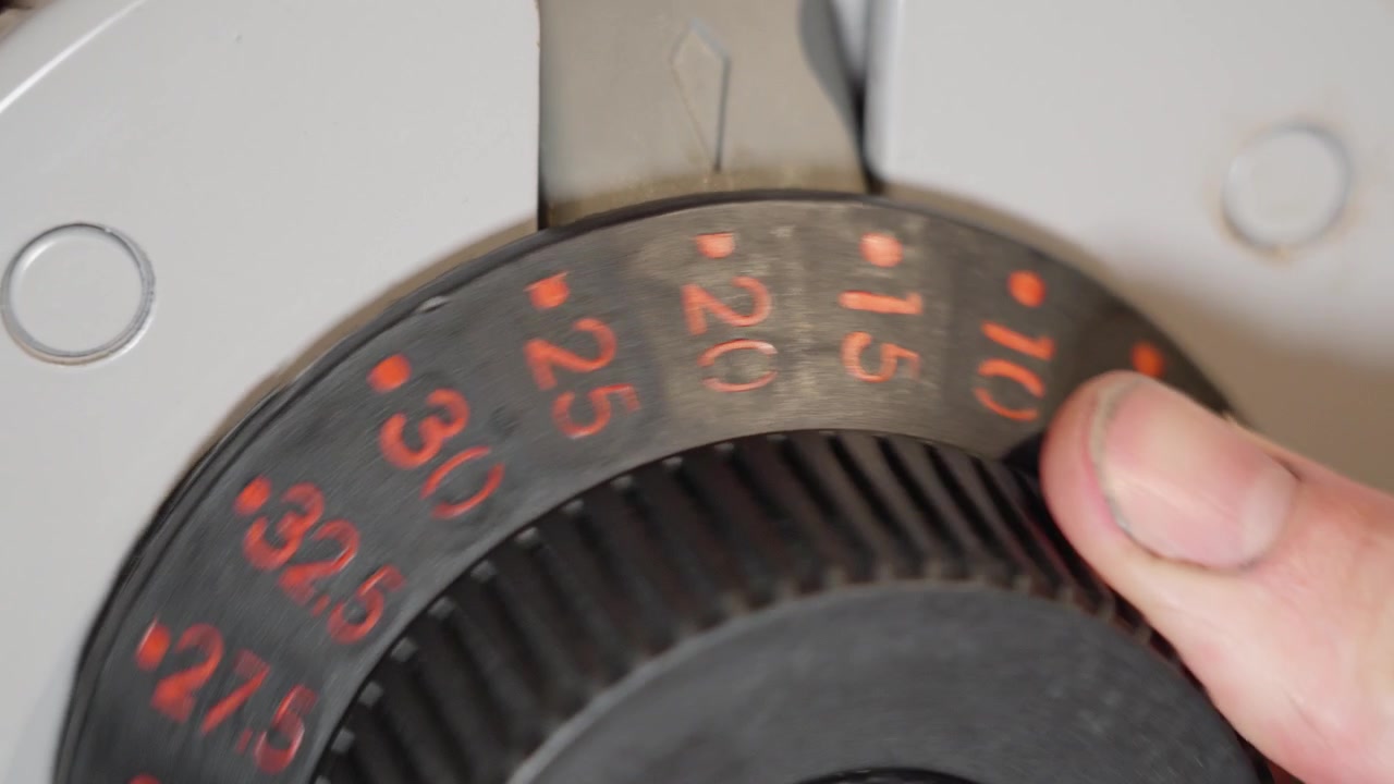 Close up of an adjustable dumbbell showing weight being reduced from 32 kilograms to 10 kilograms by a male hand
