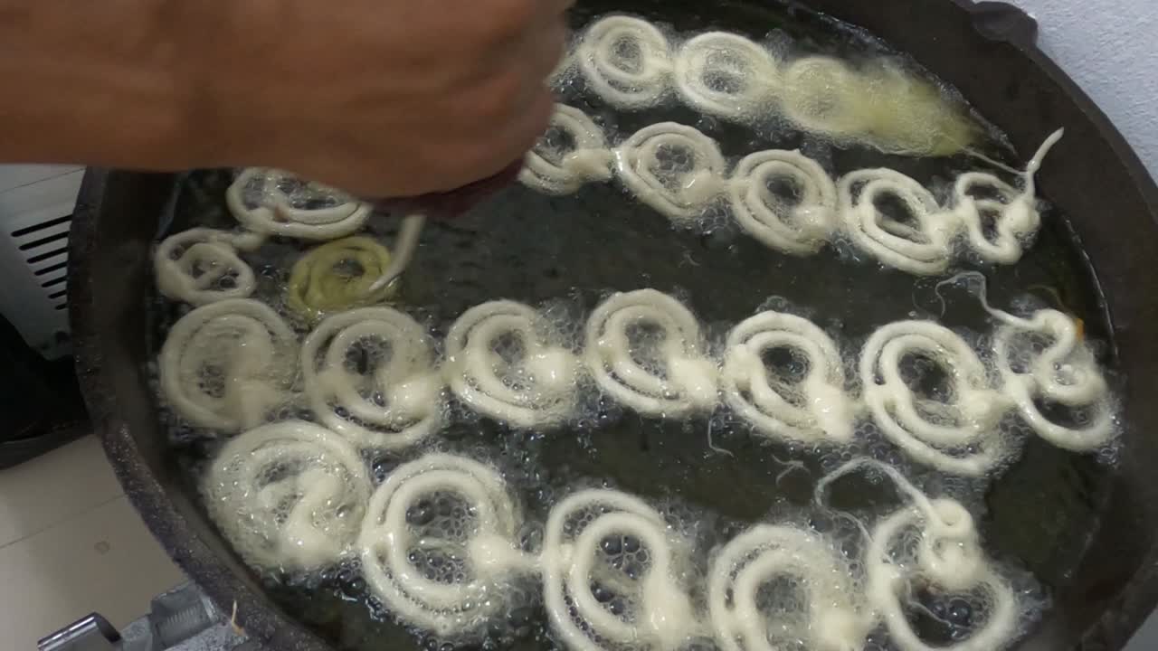 Raw jilapi deep frying 4k video clip.Jilapi making on a hot big pan.Jalebi, also known as jilapi, jilebi, jilipi, zulbia, jerry, mushabak, or zalabia, is a popular Indian sweet snack.