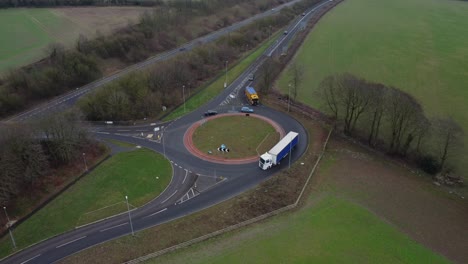 Luftdrohnenaufnahmen-Eines-Kreisverkehrs,-Der-Von-Autos-Genutzt-Wird,-Umgeben-Von-Grünen-Wiesen