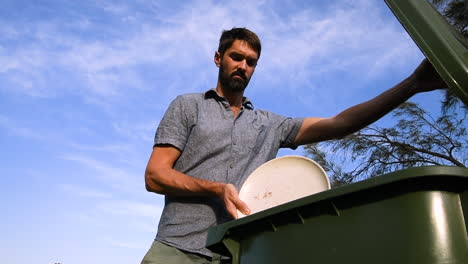 Man-wastes-plate-of-food-by-discarding-in-bin,-low-angle-outside-shot