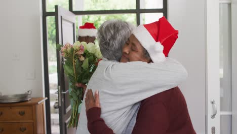 two diverse senior female friends welcoming in doorway at christmas time