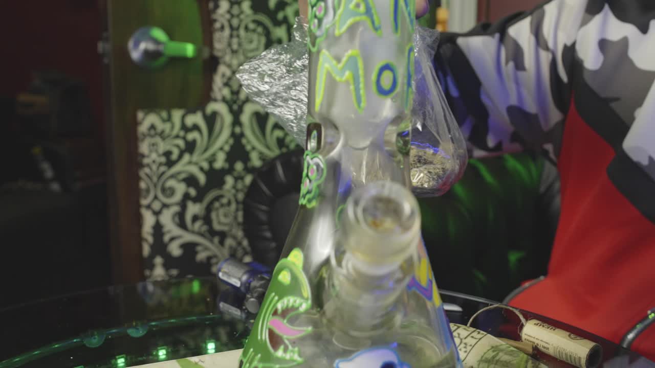 흑인 남자가 마리화나 한 봉투를 들고, 을 제거하고, 마리화나는 마약을 담배를 피우기 위해 물 에 넣기 전에 새를 맡는다.