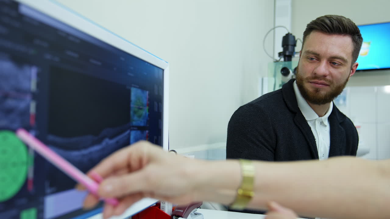 Handsome man listens to a doctor. Doctor explains something to a patient showing on the screen of a computer in medical office.