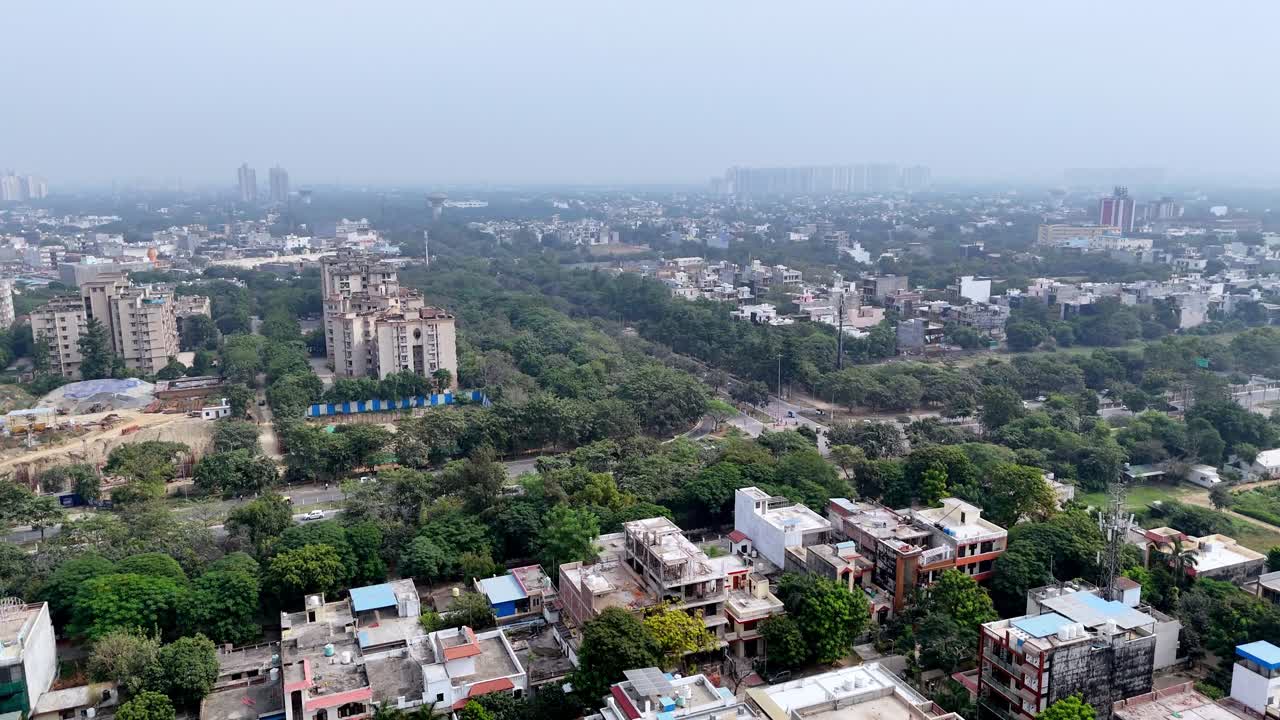Una vista con drone della fascia residenziale di Noida mostra fabbriche, aree verdi e strade arteriose che sfumano nello smog, evidenziando un rapido sviluppo sotto cieli inquinati.