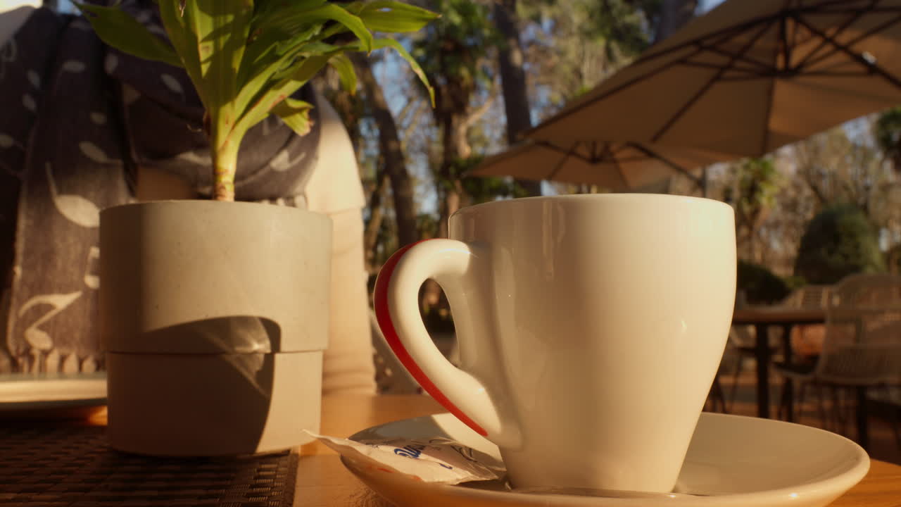 Mano che raccoglie una tazza di caffè su un tavolo da esterno di un bar