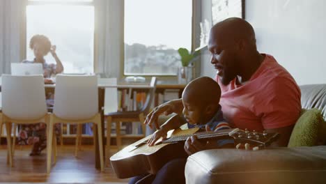 father teaching his son how to play guitar at home 4k