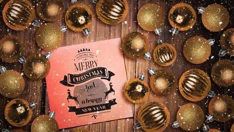 Falling-snow-and-Merry-Christmas-text-note-and-bauble-decorations-on-wood
