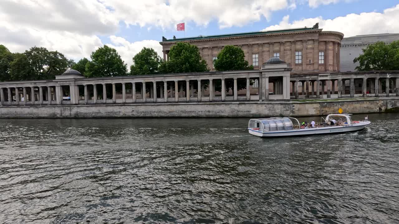 A sightseeing boat glides along the Spree River in Berlin, passing a neoclassical museum under daylight with steady camera framing and soft natural lighting