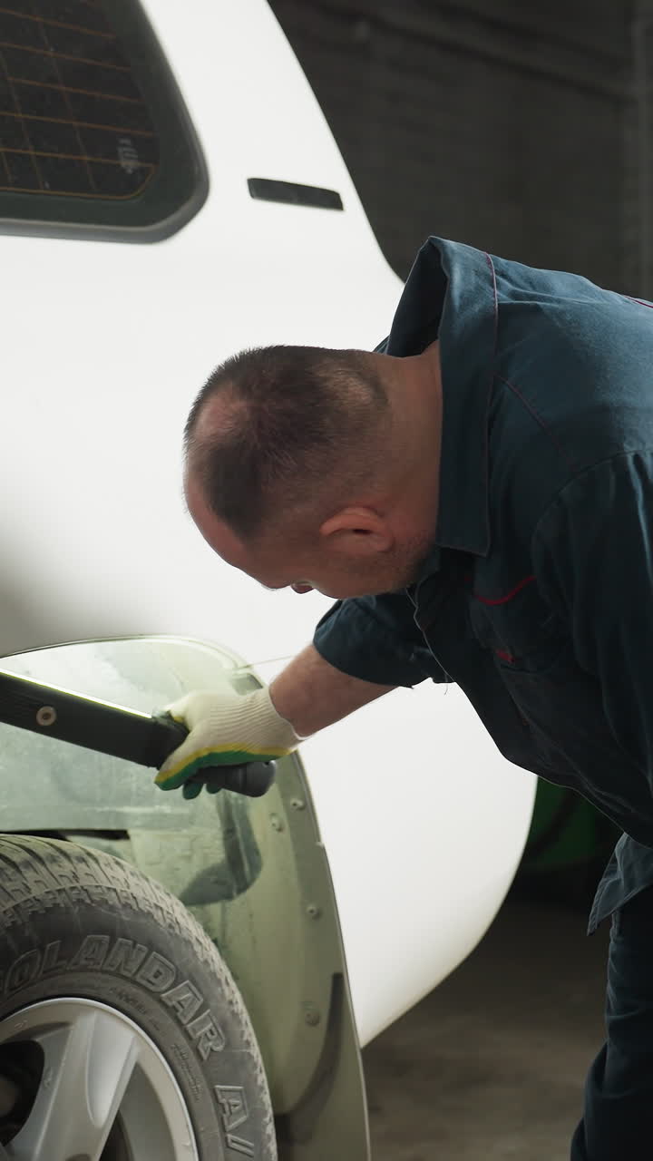 기계 작업장에서 색 지프의 타이어를 점검하는 엔지니어, 한 무을 구부리고 작업장 장비의 일부로 배경에 파란색 기둥을 가진 불 조명을 사용합니다.