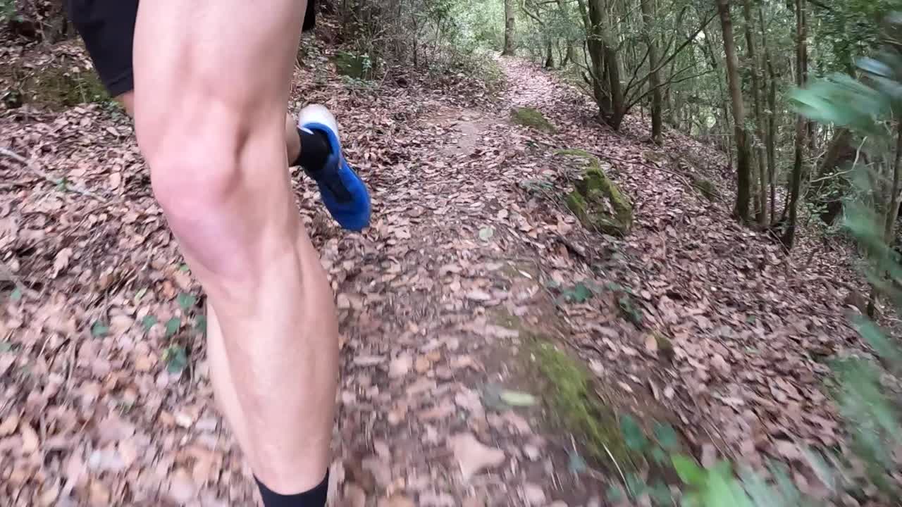 piernas musculosas y fuertes de un hombre blanco practicando trail running, en cámara lenta corriendo por un sendero, vista frontal de calzado azul y blanco