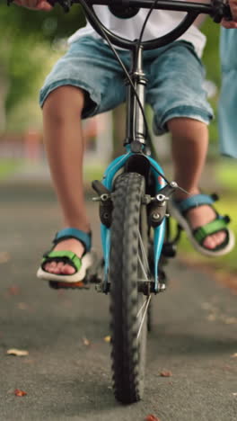 una vista de ángulo bajo de un niño montando una bicicleta, con una mujer siguiendo y apoyándolo de cerca