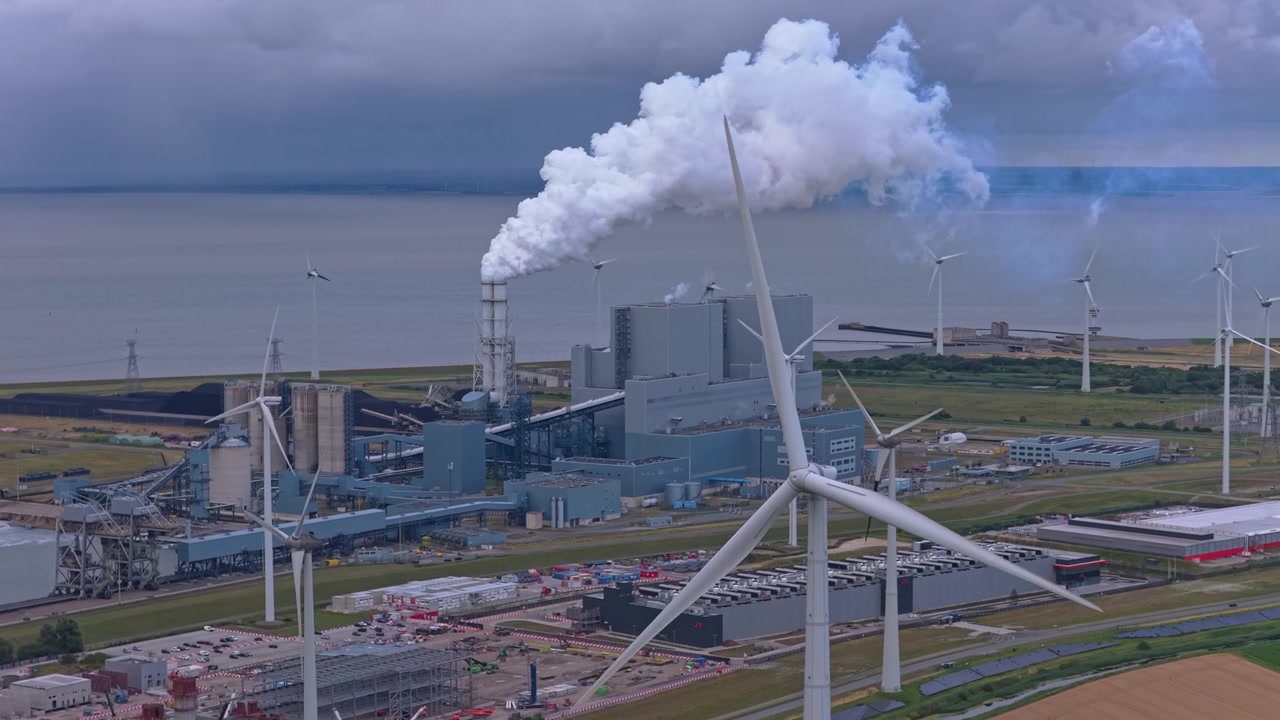 Industrikraftverk med røykutlipp omgitt av vindturbiner