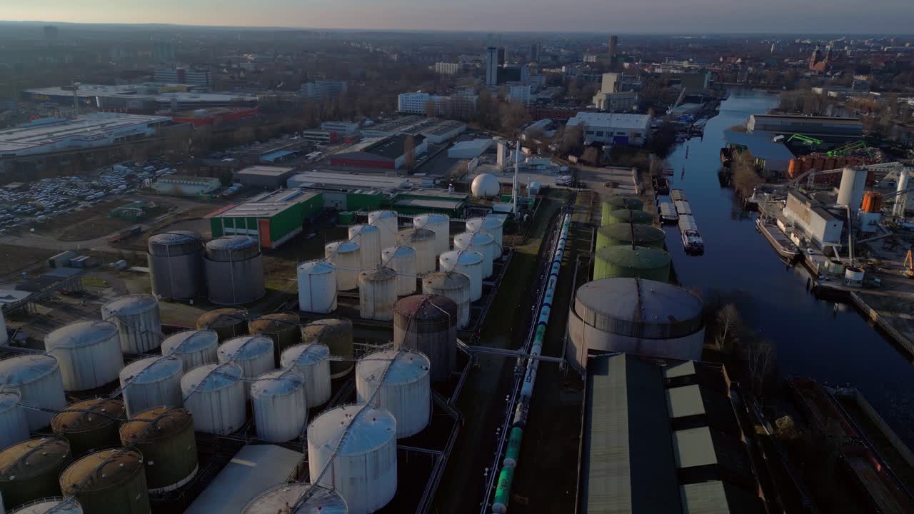 Berlin biogas plant with its large white tanks reflecting on the river next to it during sunset. Great aerial view flight static tripod hovering drone