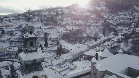 Flying-backwards-and-revealing-Old-Castle-tower-covered-by-snow-in-Mining-town-Banska-Stiavnica,-Aerial-shot