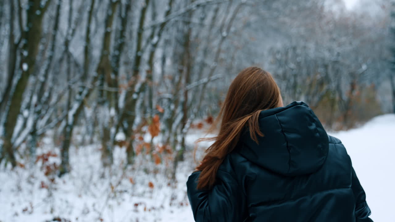Young dark-haired woman in black jacket outdoors in winter. Lady turns around touching her long hair.