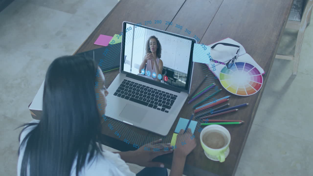Video chatting on laptop with digital data overlay, woman in home office