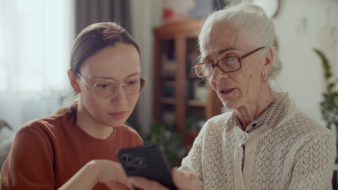 Giovane donna che insegna all'anziana nonna come usare lo smartphone a casa
